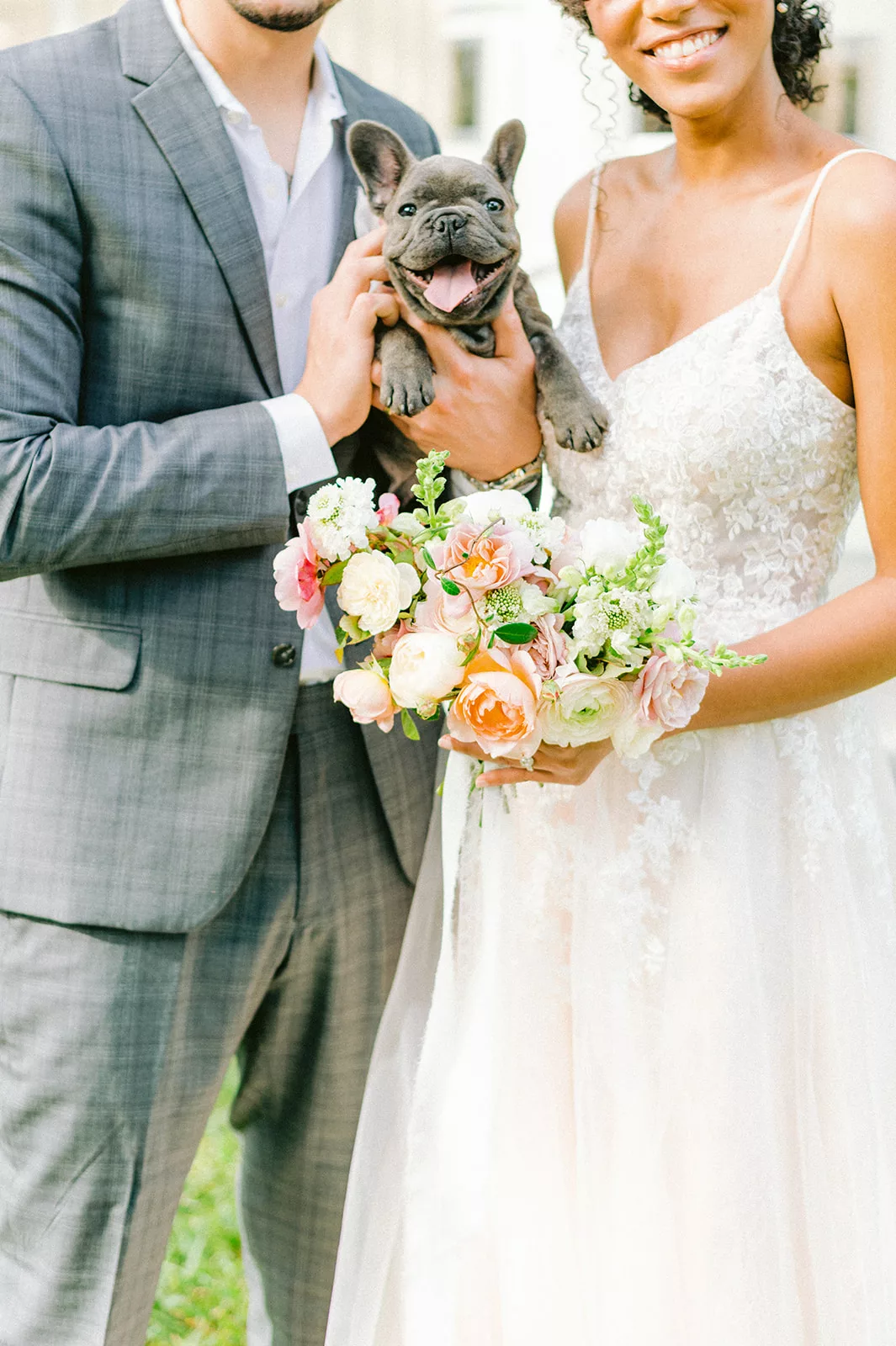 Biracial couple holding their beloved French Bulldog puppy on their wedding day - a moment of pure love and joy