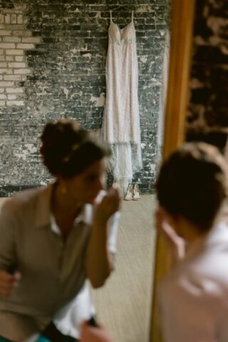 Wedding dress hanging on a brick wall with bride reflected in the mirror